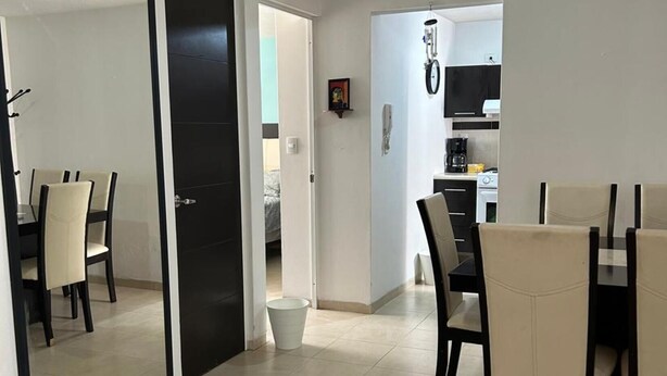 A modern living room with a dining area, a kitchen in the background, and a black door leading to another room.