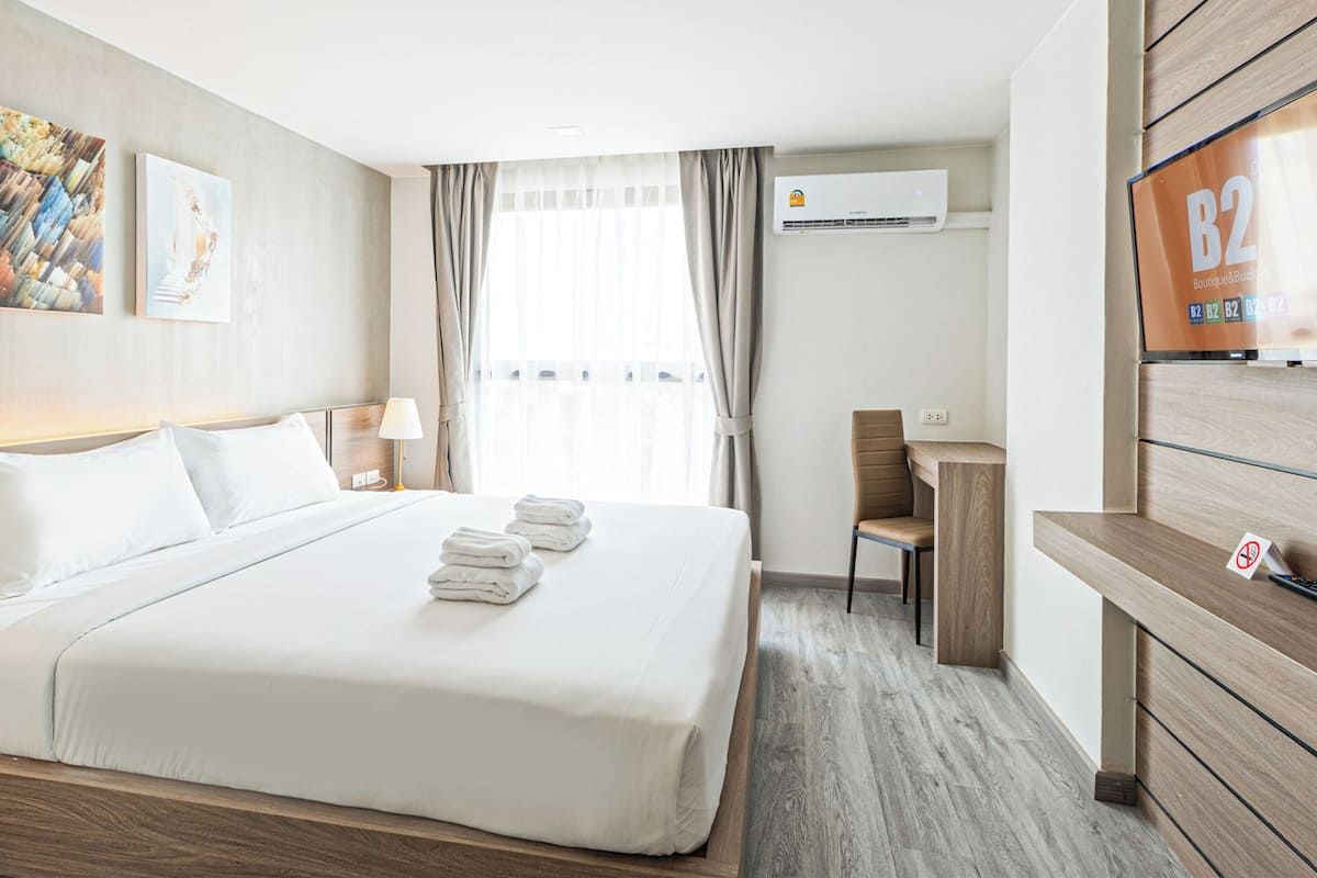 A hotel room with a large bed, a desk, a TV, and artwork on the wall.