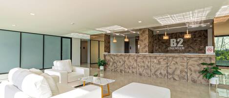 A modern lobby with a reception desk labeled "B2 PREMIER," white sofas, a marble coffee table, and potted plants.