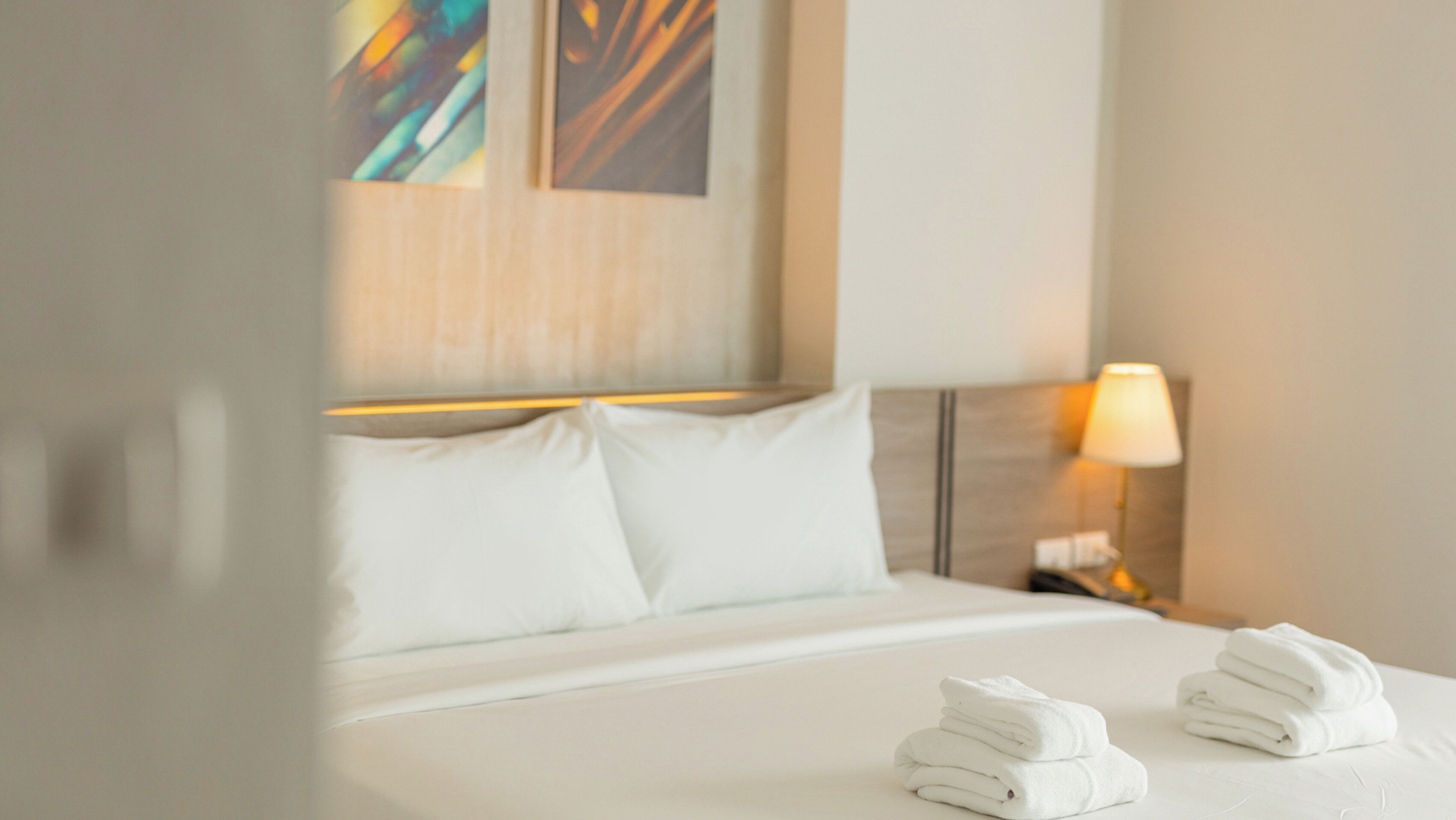 A neatly made bed with white linens and two folded towels on the side.