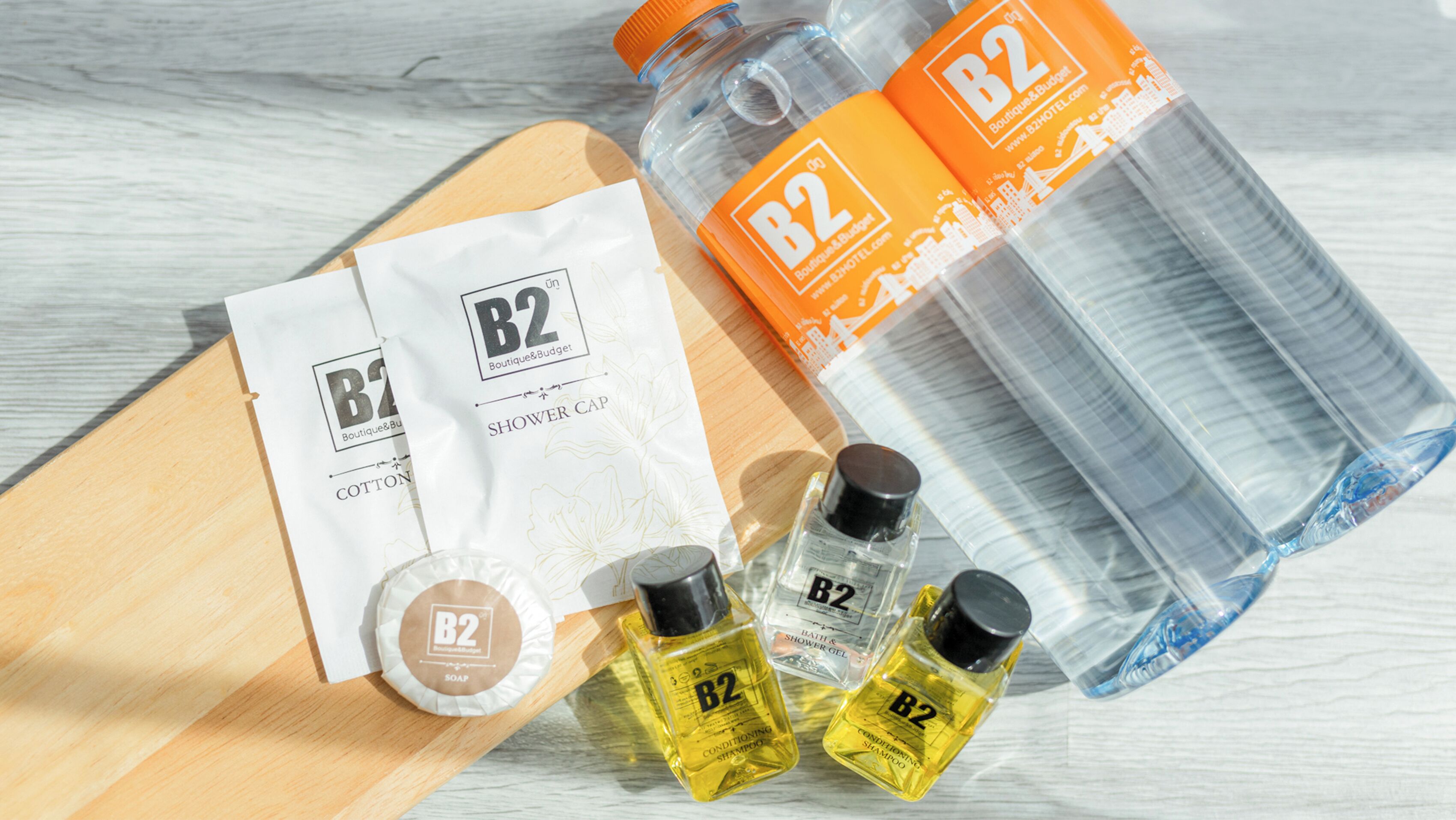 A wooden surface with various B2 branded toiletries including cotton wipes, soap, shampoo, and shower gel.