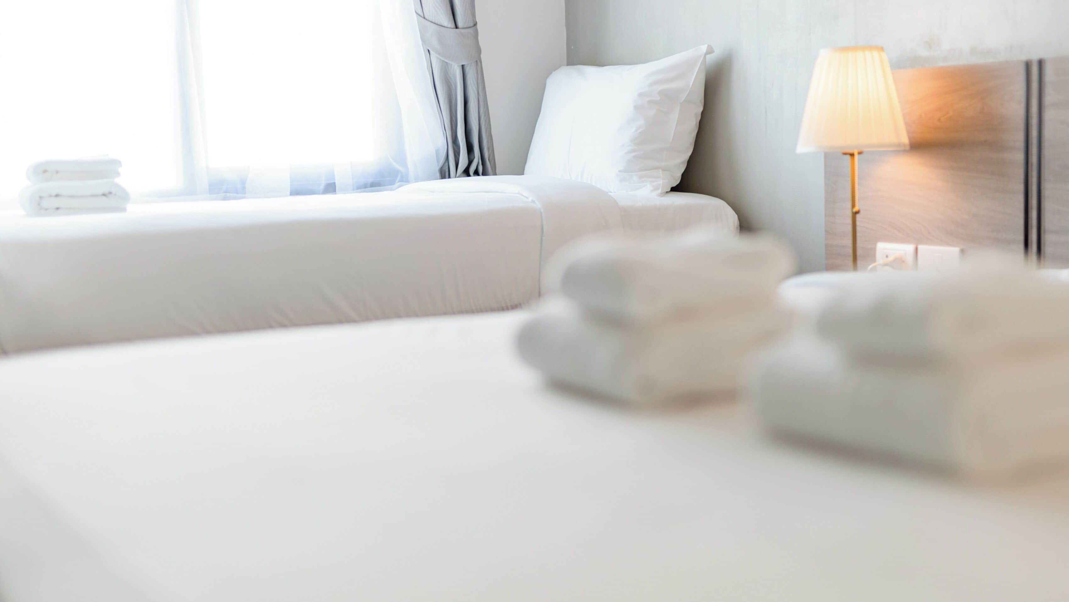 A hotel room with a bed, a bedside lamp, and a window with curtains.
