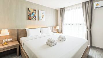 Een hotelkamer met een groot bed, twee nachtkastjes, een lamp, een wandairconditioner en een raam met gordijnen.