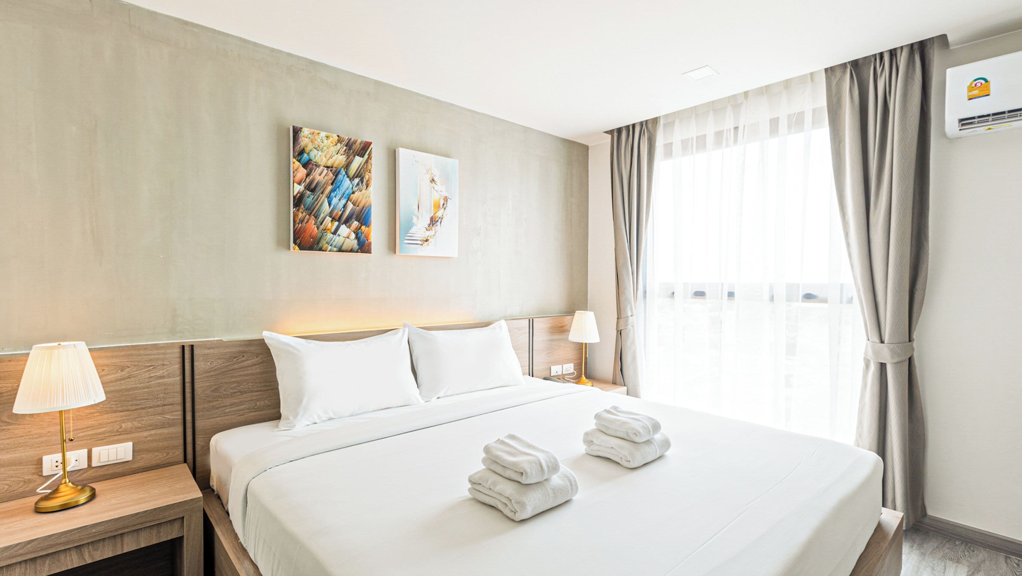 Ein Hotelzimmer mit einem großen Bett, zwei Nachttischlampen, einem Fenster mit Vorhängen und zwei Wandbildern.