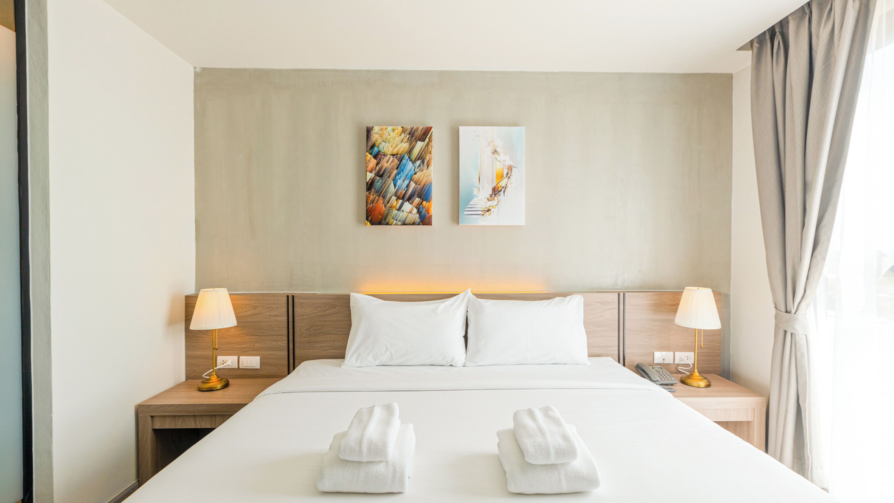 Habitación de hotel con una cama grande, dos lámparas de noche, dos cuadros en la pared y vistas al exterior.