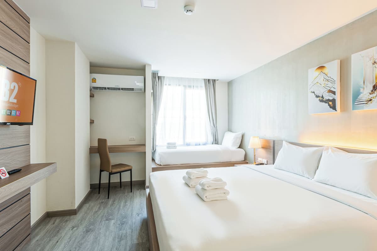 A hotel room with a bed, a desk, a chair, a TV, and artwork on the wall.