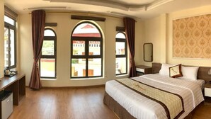A hotel room with a large bed, a TV, a desk, and a view of a building through arched windows. - Bac Ha Hotel Lao Cai- by Bay Luxury (Bac Ha)