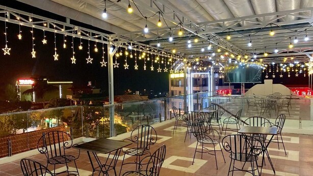 An outdoor terrace with metal chairs and tables, string lights, and a view of the city at night. - Bac Ha Hotel Lao Cai- by Bay Luxury (Bac Ha)