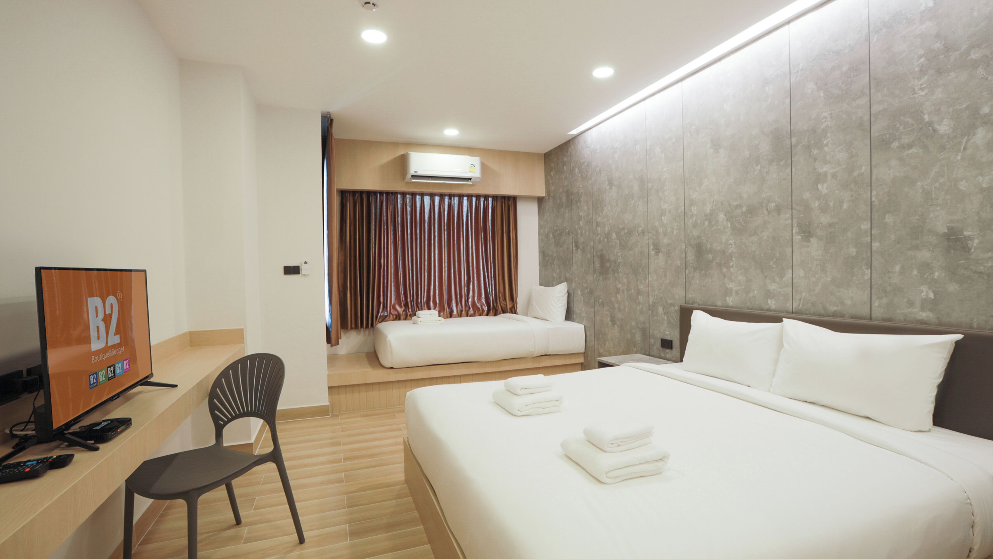 A hotel room with a bed, a desk with a computer, a chair, and a TV.