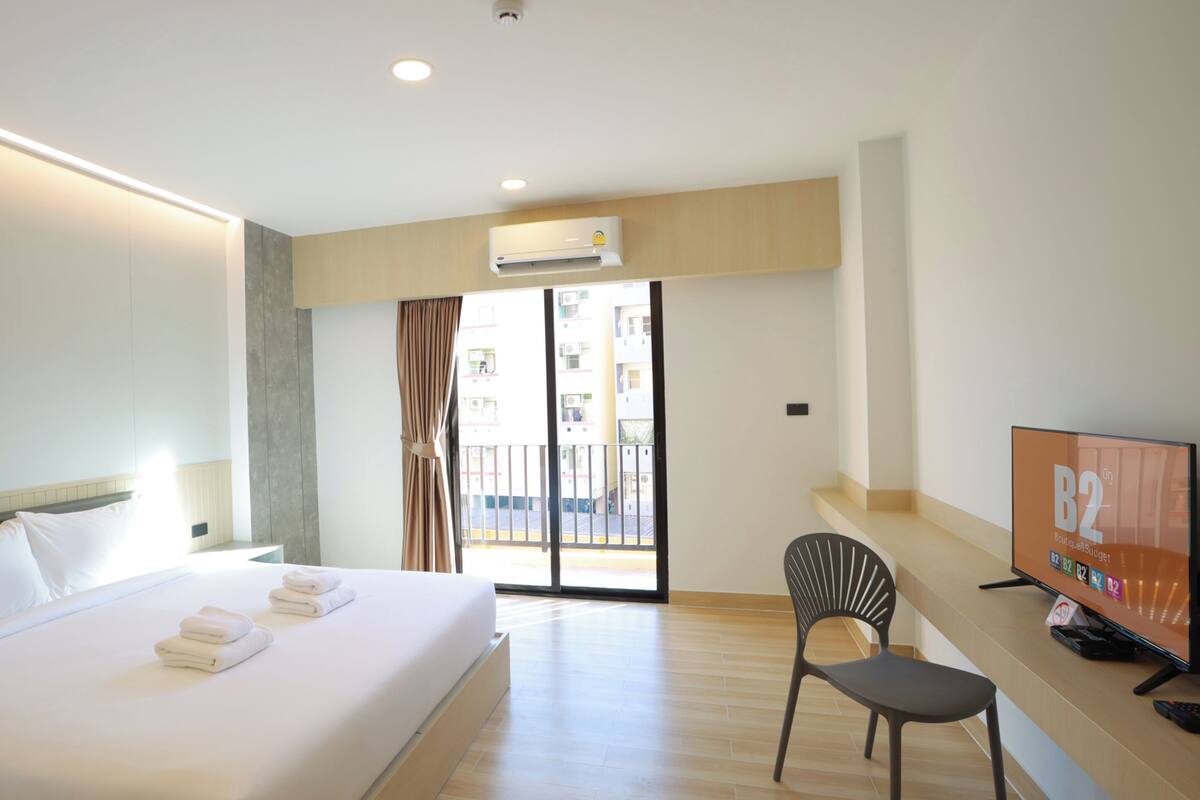 Habitación de hotel con cama, escritorio con silla, televisor y puerta corrediza al balcón.