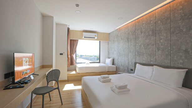 Ein modernes Hotelzimmer mit einem großen Bett, einem Schreibtisch mit Fernseher, einem Sessel und Blick auf die Stadt durch das Fenster.