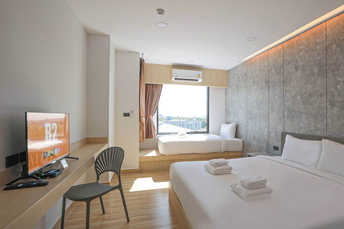 Habitación de hotel moderna con una cama grande, un escritorio con televisor, una silla y vista a la ciudad por la ventana.