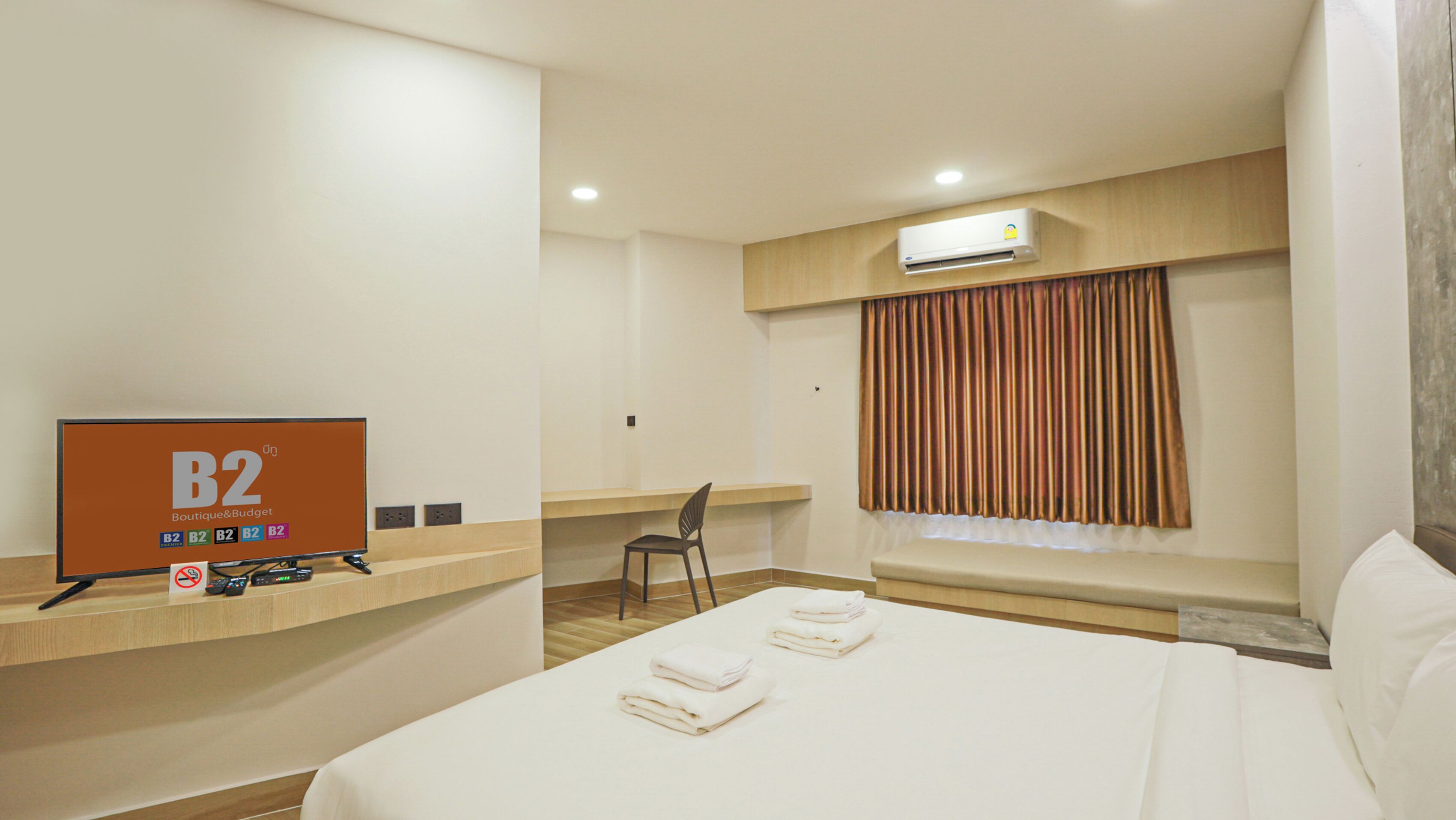 A hotel room with a bed, a desk, a chair, an air conditioner, and a sign on the wall.