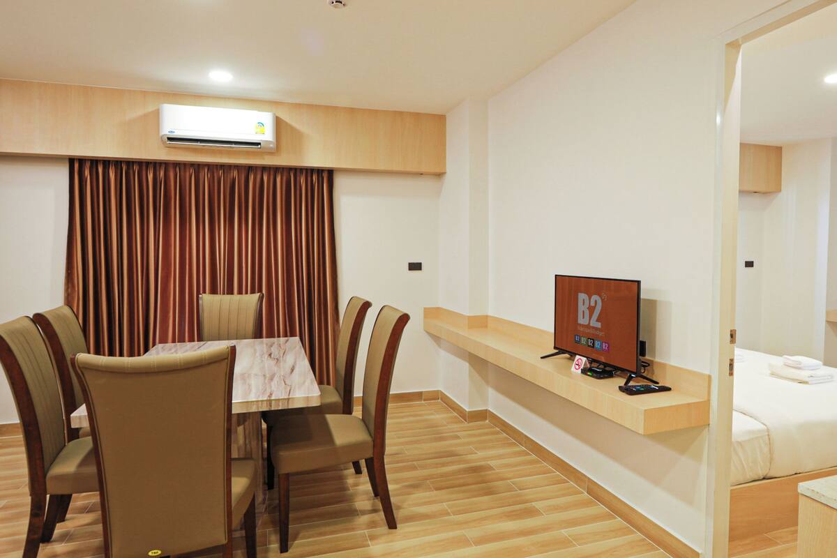 Habitación de hotel con una mesa de comedor, cuatro sillas, un televisor, una cama y un espejo.