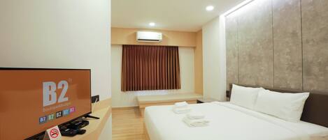 Una habitación de hotel con una cama grande, un escritorio con televisor y una ventana con cortinas.