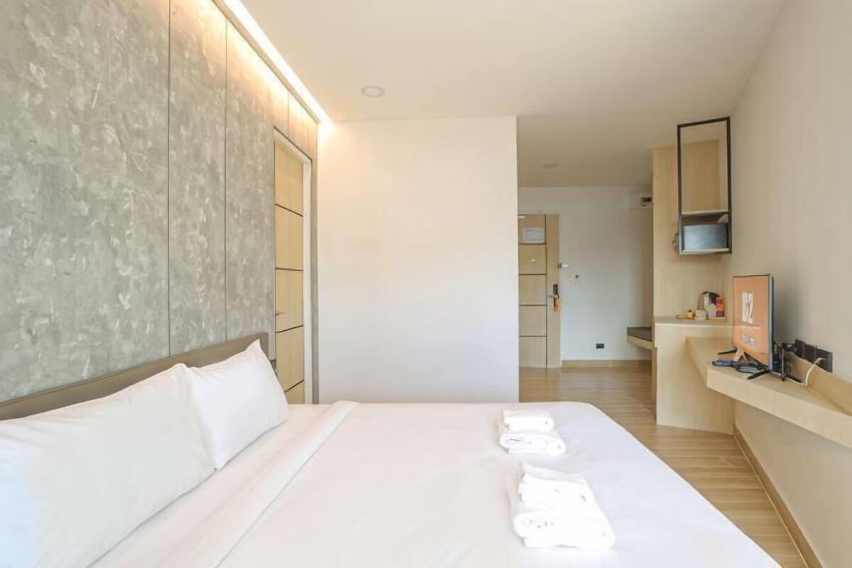 Habitación de hotel con una cama grande, una mesita de noche, un espejo y vistas al área de la cocina.