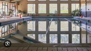 An indoor swimming pool with a view of the outdoors through large windows, wooden beams on the ceiling, and potted plants around the pool area. - Large Cozy Townhouse Ski-in / Ski-out to Super Bee, Private Washer /Dry & Garage (Frisco)
