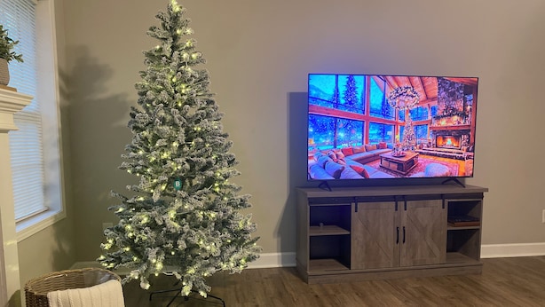 Un salon avec un sapin de Noël, un téléviseur et un meuble de rangement en bois.
