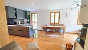 Une cuisine moderne avec des meubles gris, un coin repas avec une table et des chaises en bois, et un coin salon confortable avec un banc et un pouf.
