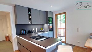 Une cuisine moderne avec des meubles gris, un îlot central et un coin repas comprenant une table et des chaises en bois.