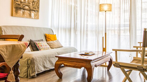 Un salon chaleureux avec un canapé, une table basse en bois, un lampadaire et un tableau représentant un paysage urbain.
