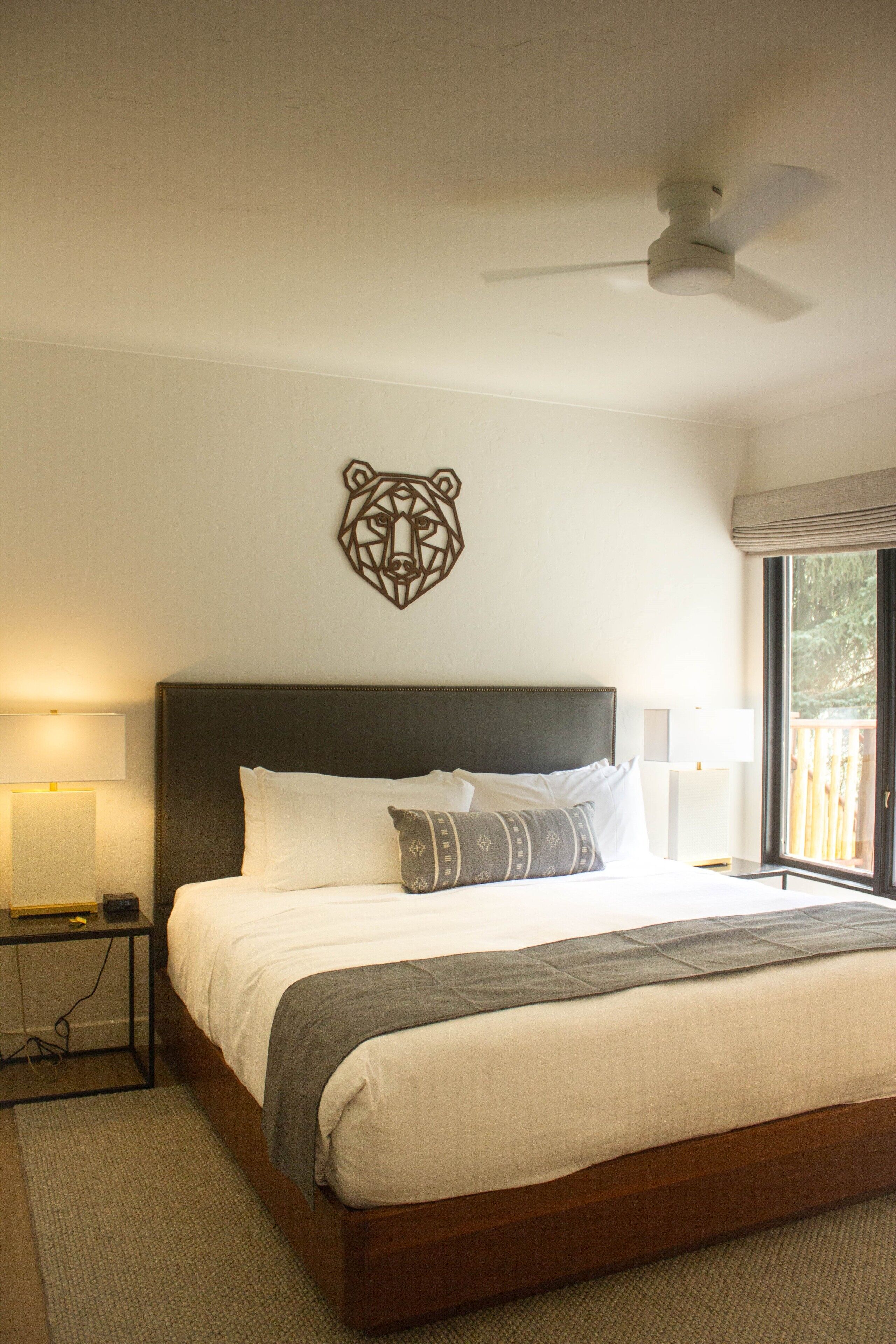A bedroom with a large bed, a ceiling fan, a wall-mounted decorative bear head, and a window with a view of the outdoors.