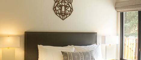 A bedroom with a large bed, a ceiling fan, a wall-mounted decorative bear head, and a window with a view of the outdoors.