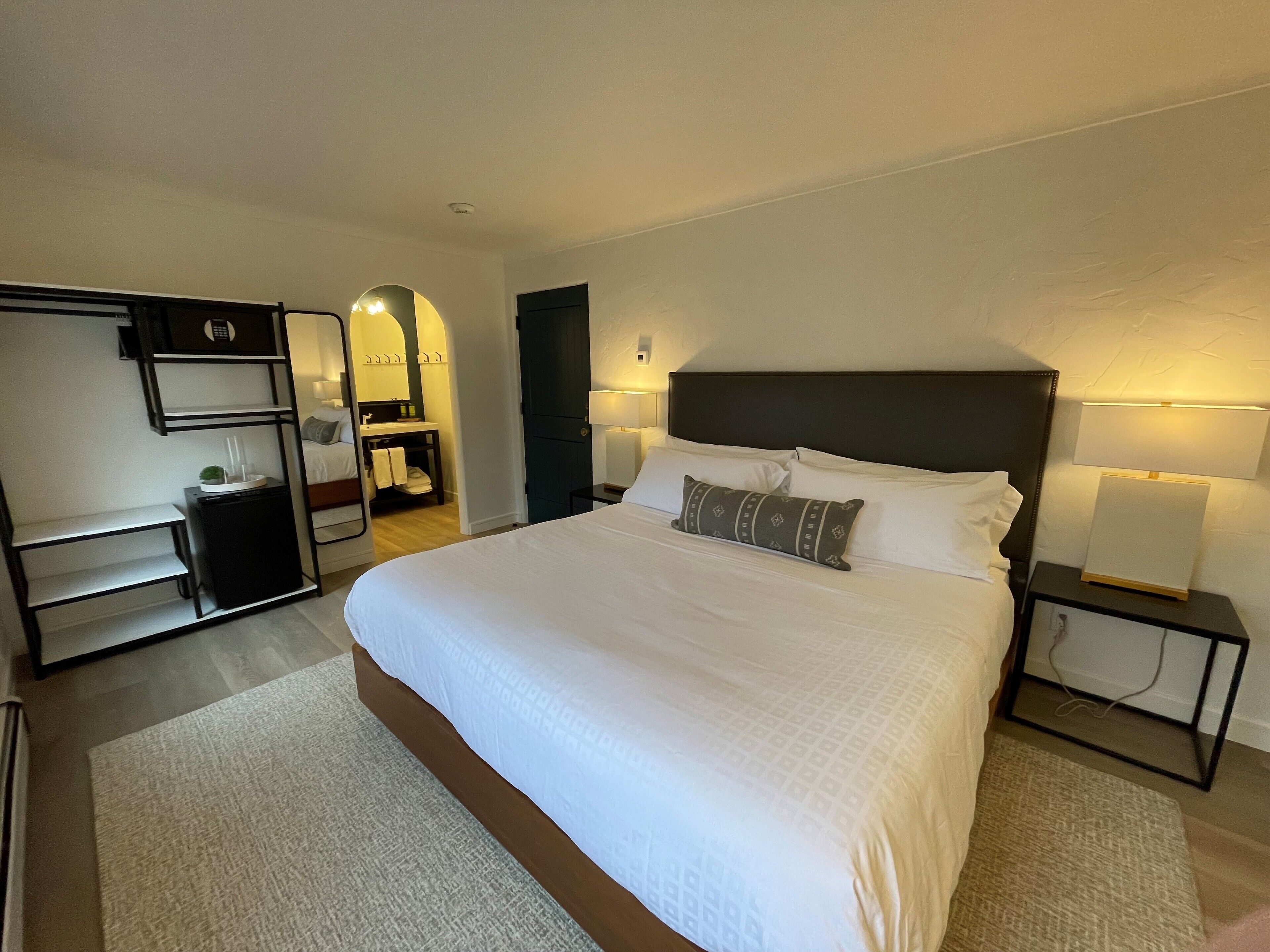A hotel room with a large bed, bedside tables with lamps, a wardrobe, and a mirror.