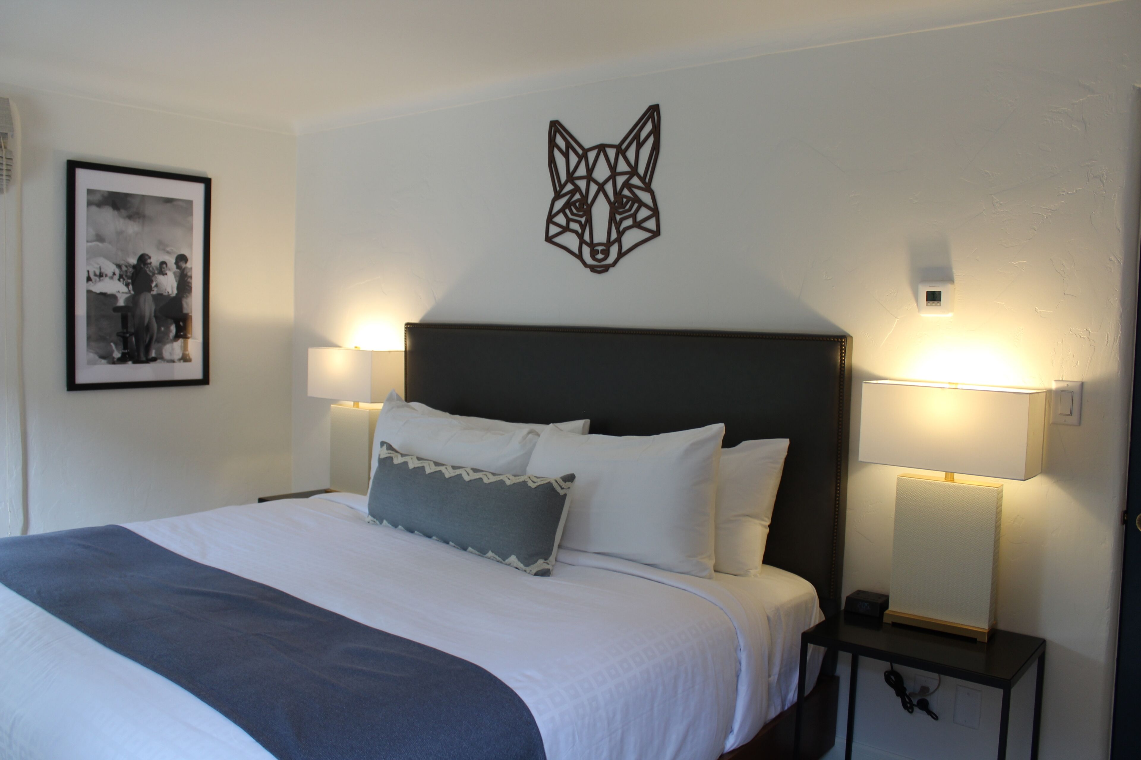 A neatly made bed with white linens and a gray throw blanket, flanked by two bedside lamps on a nightstand.