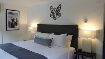 A neatly made bed with white linens and a gray throw blanket, flanked by two bedside lamps on a nightstand.