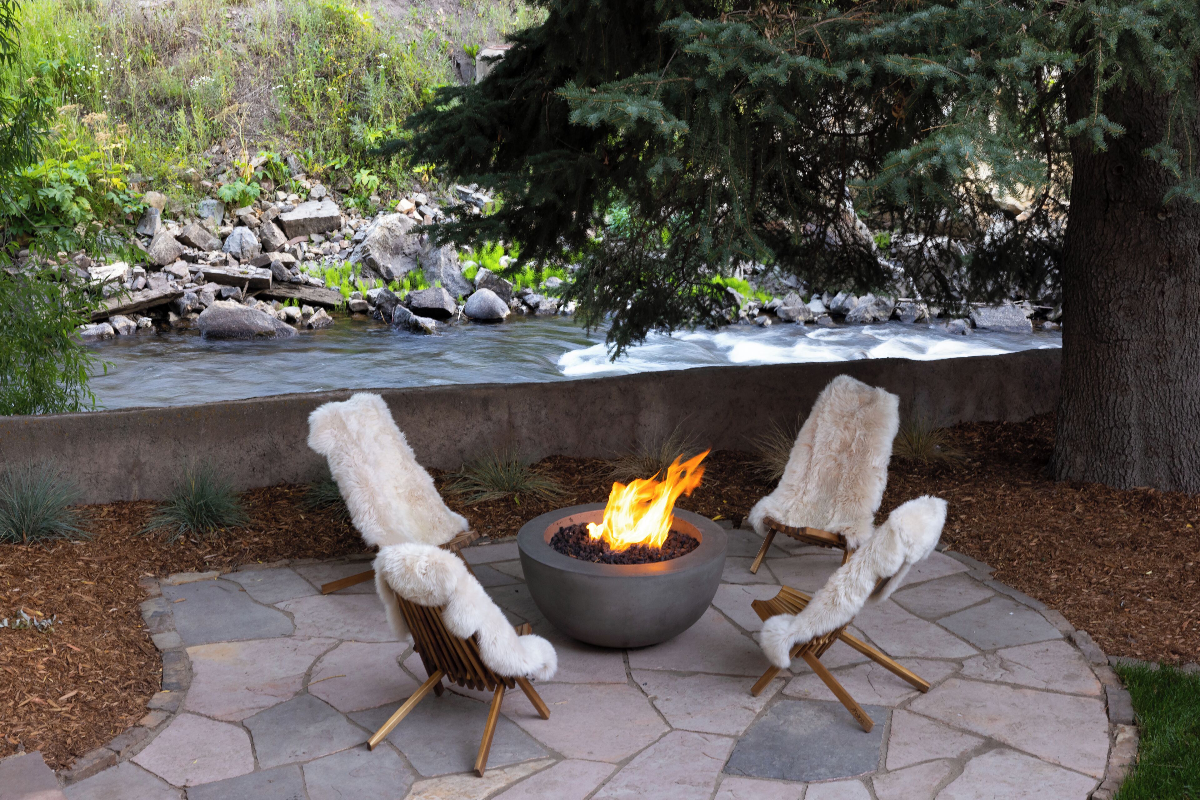 A stone patio with a central fire pit and two fur-covered chairs.
