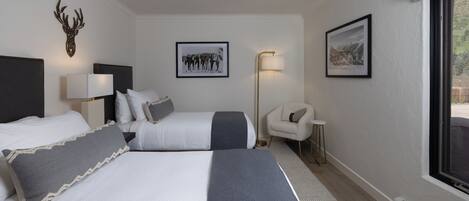 A hotel room with two beds, a nightstand with a lamp, a chair, and framed pictures on the wall.