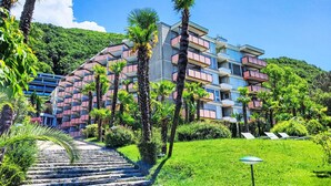 A multi-story hotel with balconies, surrounded by lush greenery and a clear blue sky.