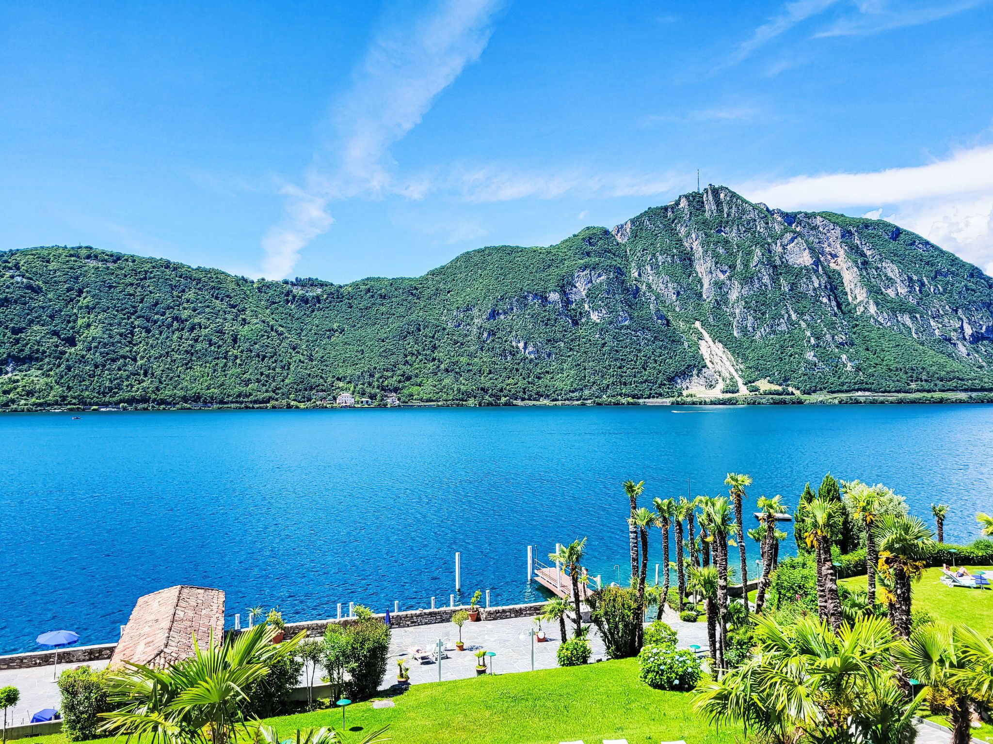 Un complejo turístico en la costa con vista a una montaña y un lago azul cristalino.