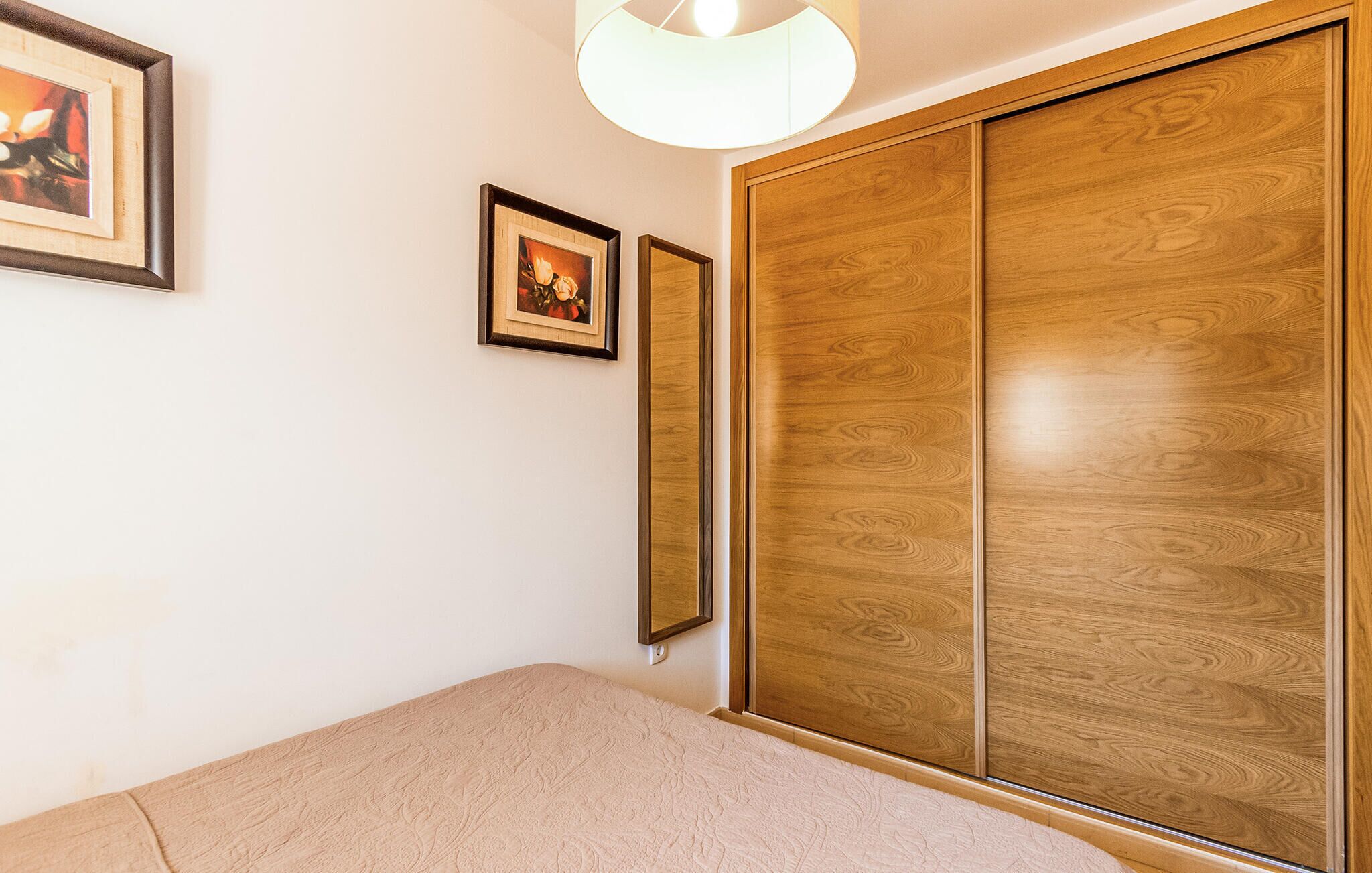A bedroom with a bed, a wooden wardrobe, and two framed pictures on the wall.