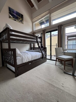 Una cama litera con una silla y una mesa en una habitación con un ventanal grande y un cuadro en la pared.