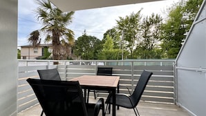A balcony with a table and chairs, a palm tree, and a view of a street and buildings. - Residence Eva 4 - Carraro Immobiliare Jesolo (Cavallino-Treporti)