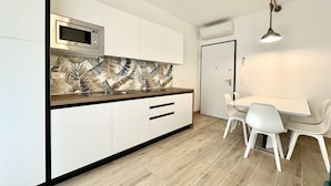 A modern kitchen with white cabinets, a microwave, and a patterned backsplash. There is a dining table with chairs and a pendant light. - Residence Eva 4 - Carraro Immobiliare Jesolo (Cavallino-Treporti)