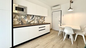 A modern kitchen with white cabinets, a microwave, and a patterned backsplash. There is a dining table with chairs and a pendant light.
