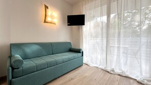 A teal sofa in a room with a large window, a wall-mounted TV, and a light fixture.
