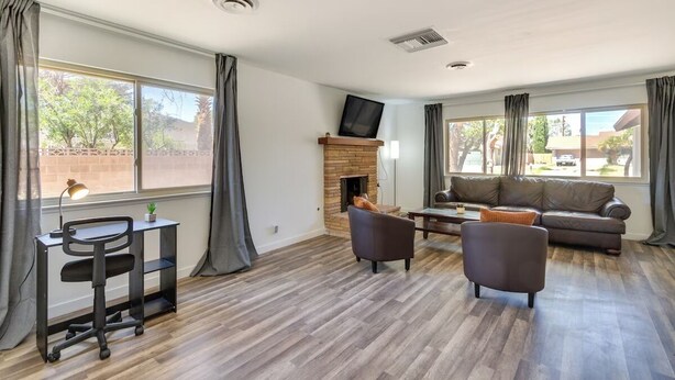 A spacious living room with a fireplace, a sofa, a desk, and a TV mounted on the wall. - Peaceful & Modern Ridgecrest Retreat: Spacious 4-Bed Home w/ Private Yard (Ridgecrest)