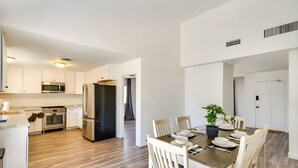 A modern kitchen with stainless steel appliances, a dining area with a wooden table and white chairs, and a hallway leading to a door. - Peaceful & Modern Ridgecrest Retreat: Spacious 4-Bed Home w/ Private Yard (Ridgecrest)
