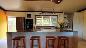 Een moderne keuken met een centraal eiland, barkrukken, een raam met zonwering en een inbouwoven.
