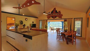 Een moderne keuken met een centraal eiland, een eetgedeelte met houten stoelen en een groot raam met gordijnen.
