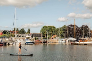 A marina with boats docked, a person paddleboarding, and buildings in the background.