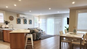 A modern kitchen with a central island, a dining area with a table and chairs, and a living area with a sofa and a coffee table.