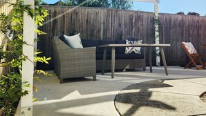 A covered patio area with a white pergola, a wicker sofa, a small table, and a wooden fence in the background.