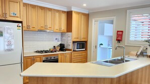 A modern kitchen with wooden cabinets, a central island with stools, a built-in microwave, and a stainless steel sink.