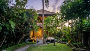 A traditional building with a thatched roof, surrounded by lush greenery and a well-maintained garden. - Villa Sujati (Ubud)