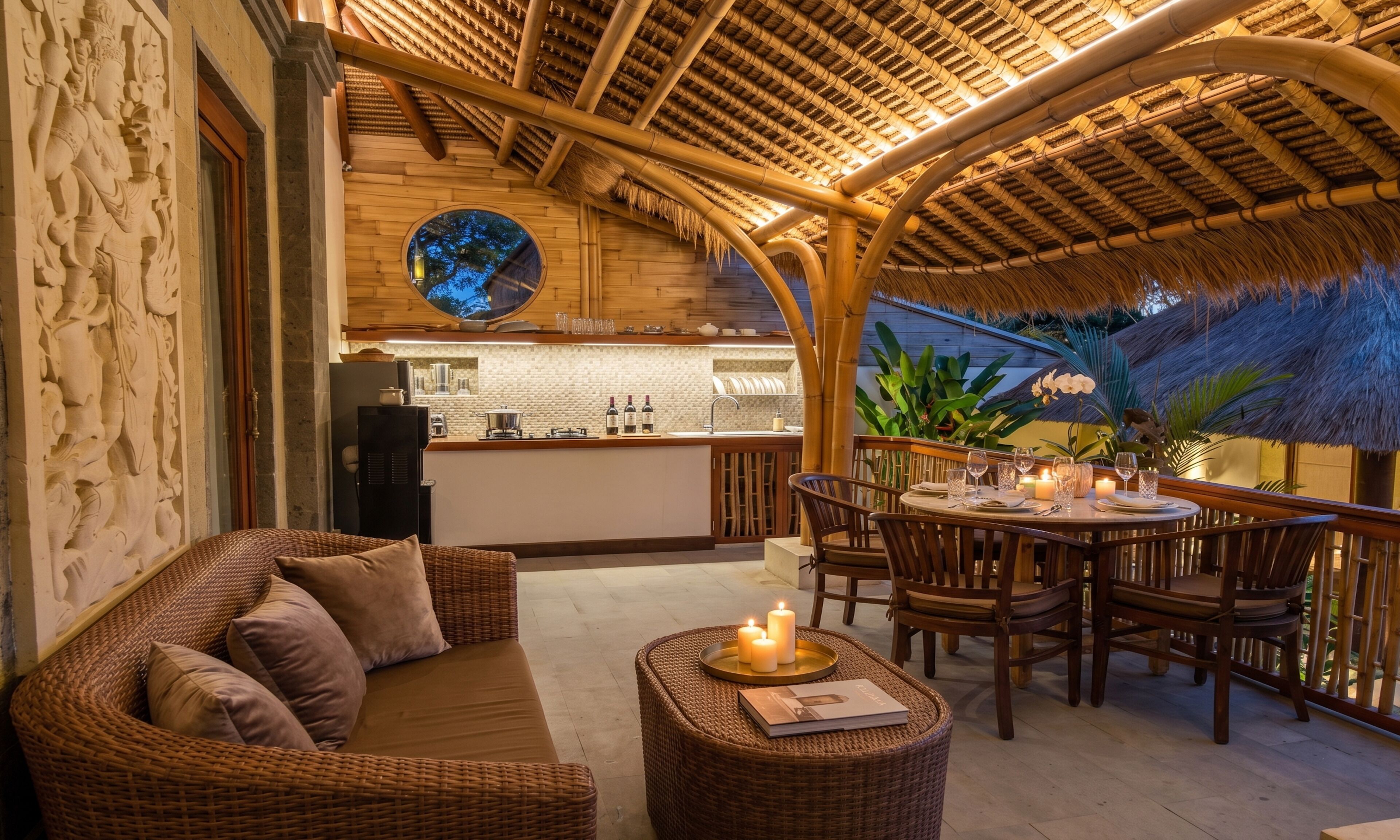 Un espace de détente extérieur accueillant, avec des meubles en osier, une table ronde décorée de bougies et une cuisine en arrière-plan.